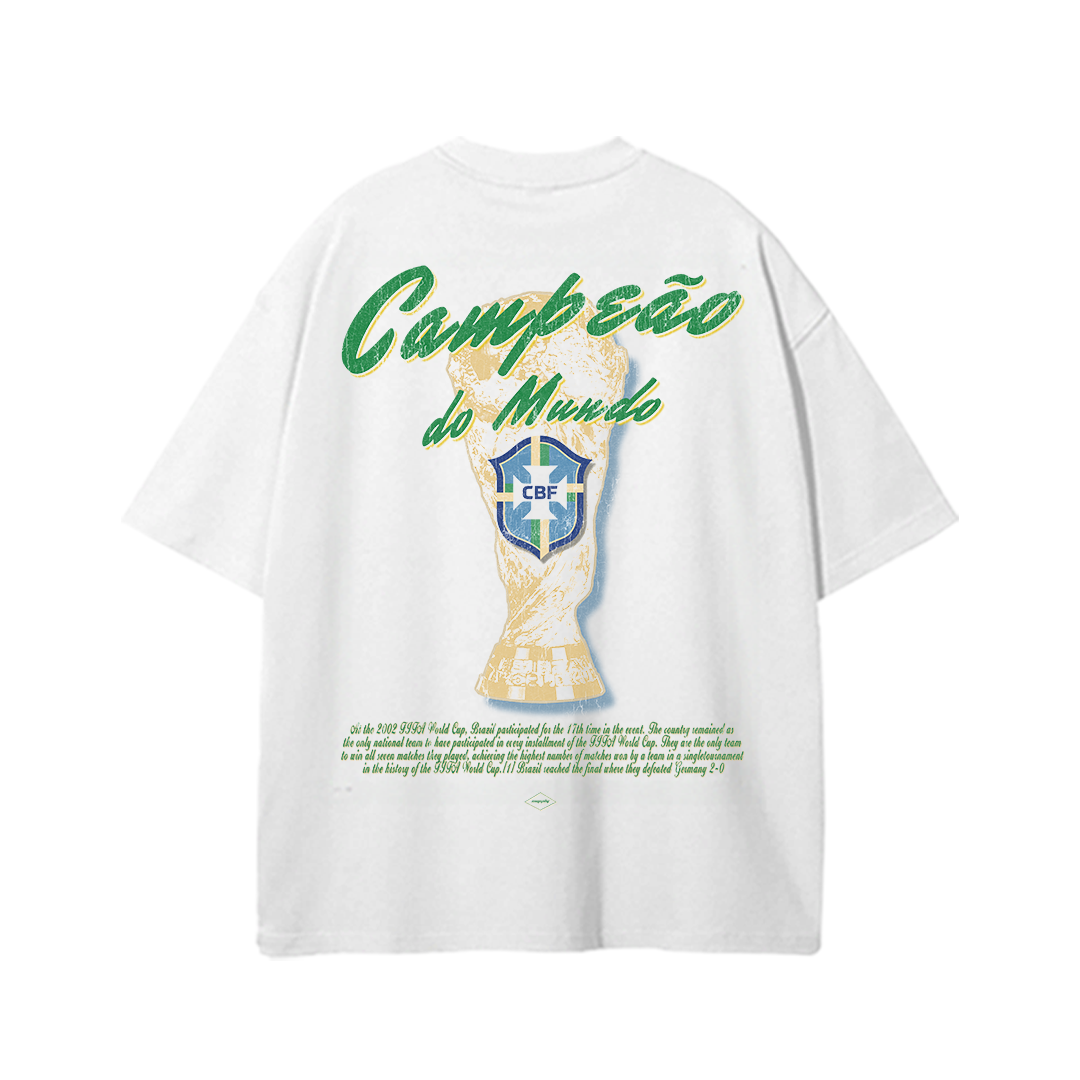 White oversized Brazil World Cup t-shirt featuring gold trophy artwork, CBF crest, and green “Campeão do Mundo” typography inspired by vintage Brazilian football culture.