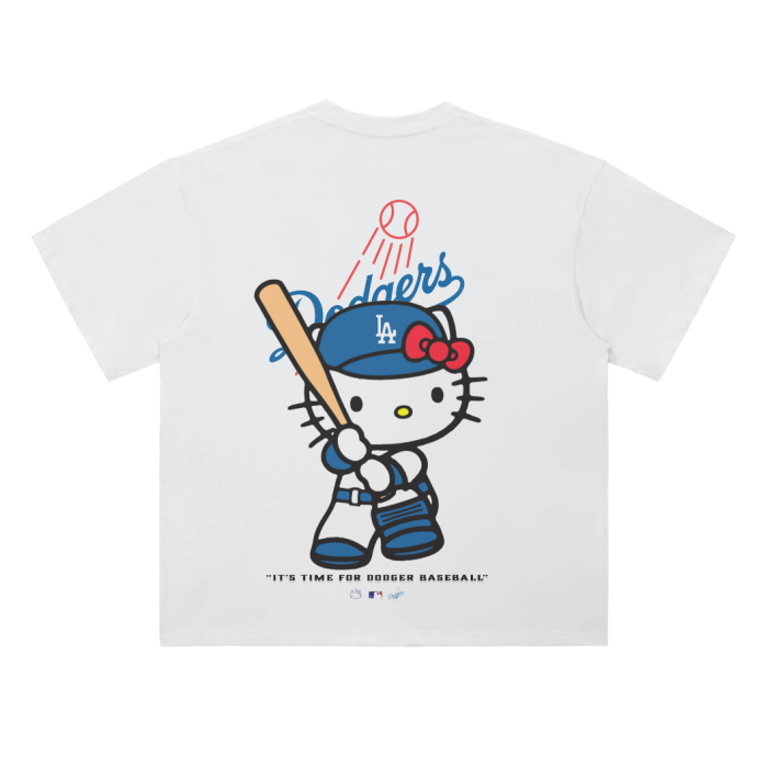 A white T-shirt featuring an illustration of Hello Kitty dressed in a Los Angeles Dodgers uniform holding a baseball bat, with the Dodgers logo above her and the phrase "It's Time For Dodger Baseball!" below