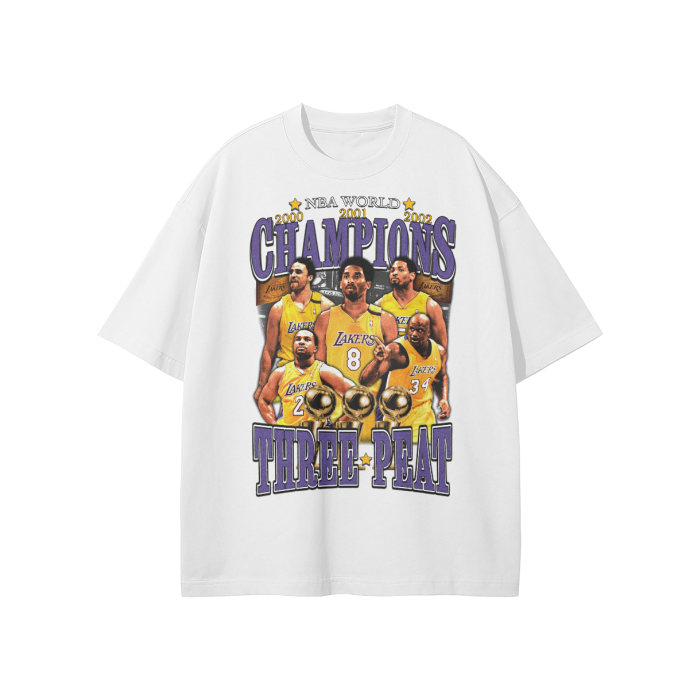 A white oversized T-shirt featuring the Los Angeles Lakers’ three-peat NBA championships. The front design includes portraits of key players like Kobe Bryant and Shaquille O'Neal with the text "NBA World Champions Three-Peat" in purple and gold.