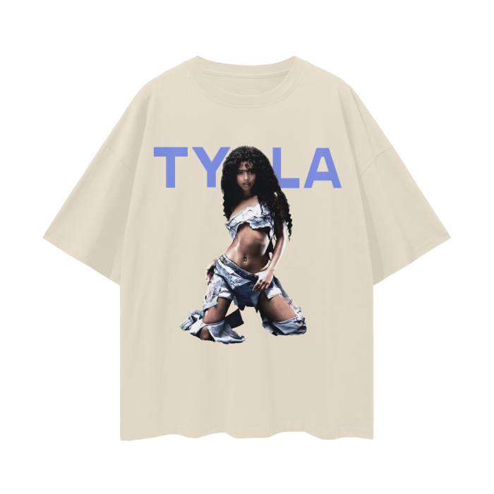 A beige oversized t-shirt featuring a bold image of Tyla, a prominent music artist. The design showcases Tyla in a striking pose, wearing a denim-inspired outfit that is edgy and stylish. Above her image, the text "TYLA" is displayed in large, bold blue letters, creating a modern and eye-catching graphic.