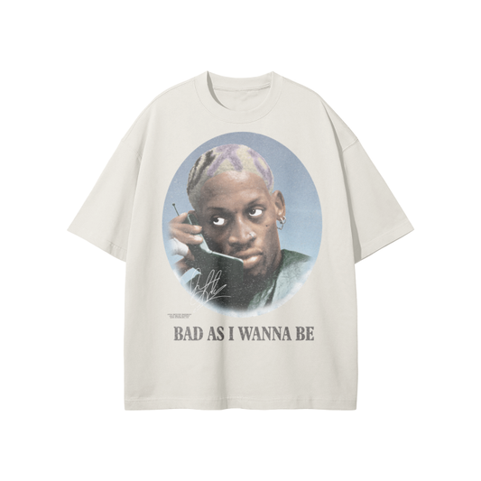 Vintage-style oversized t-shirt featuring a portrait of Dennis Rodman with purple and blonde hair, holding a phone. The text below reads 'BAD AS I WANNA BE' in a bold serif font.