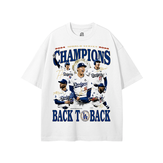 White heavyweight T-shirt with a dynamic front graphic celebrating the Dodgers’ 2024 and 2025 World Series wins. The design includes the phrase “2024 WORLD SERIES 2025 CHAMPIONS” in bold red and blue text. Below, a collage of Dodgers players in uniform—mid-action and overlaid with gold signature effects—centers the shirt. At the bottom, the words “BACK TO BACK” flank the LA Dodgers logo in a commemorative seal.