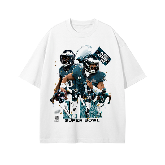 White oversized drop-shoulder T-shirt featuring a high-energy graphic of Jalen Hurts, Saquon Barkley, and other Philadelphia Eagles players celebrating their Super Bowl win. The design includes the Lombardi Trophy, a 'Fly Eagles Fly' flag, and a bold 'Super Bowl' text at the bottom, creating a dynamic and spirited look