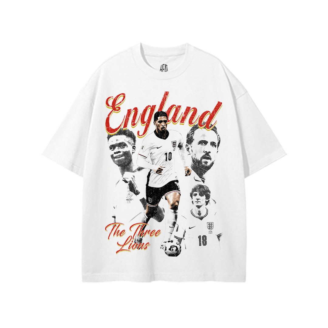 White heavyweight oversized England soccer graphic t-shirt featuring Jude Bellingham in action with monochrome portraits of Harry Kane, Bukayo Saka, and Kobbie Mainoo. Large vintage-style "England" lettering appears above with "The Three Lions" script below in red and gold accents.