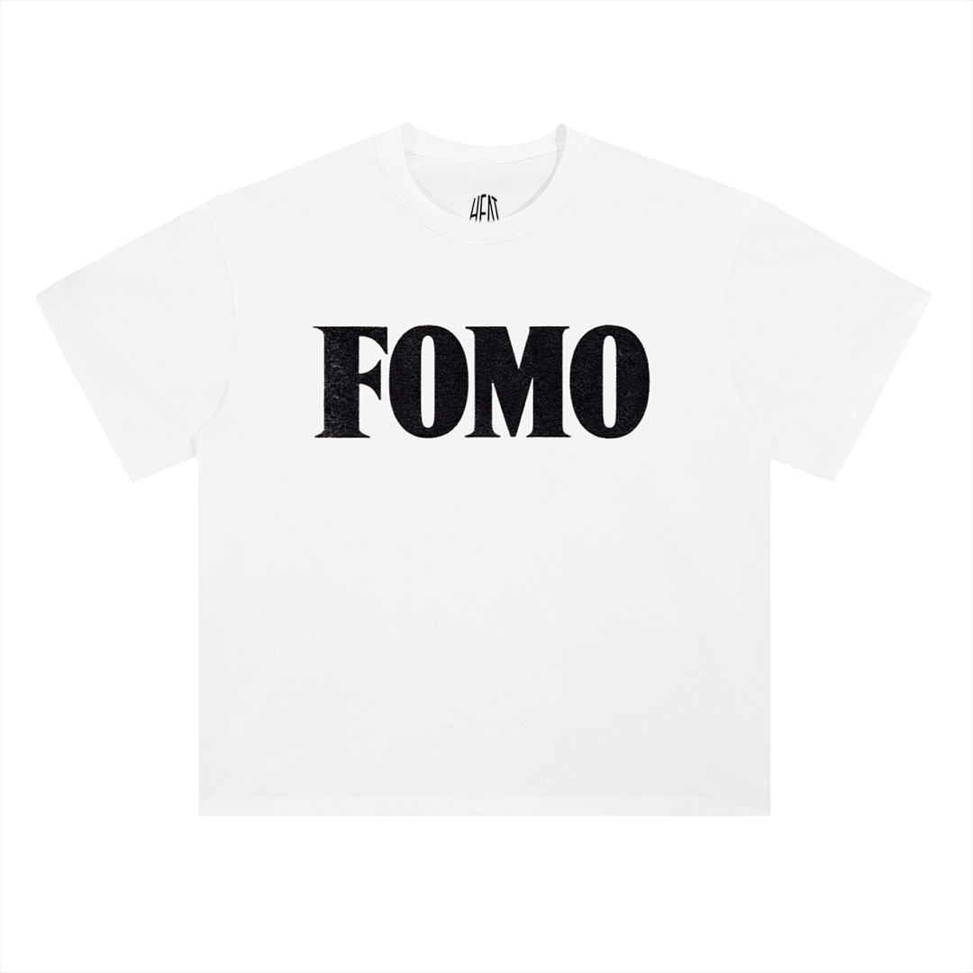 White heavyweight cotton T-shirt featuring a minimalist "FOMO" chest graphic on the front and a bold oversized "Fear Of Missing Out" typography design across the back, inspired by modern hip-hop streetwear aesthetics.