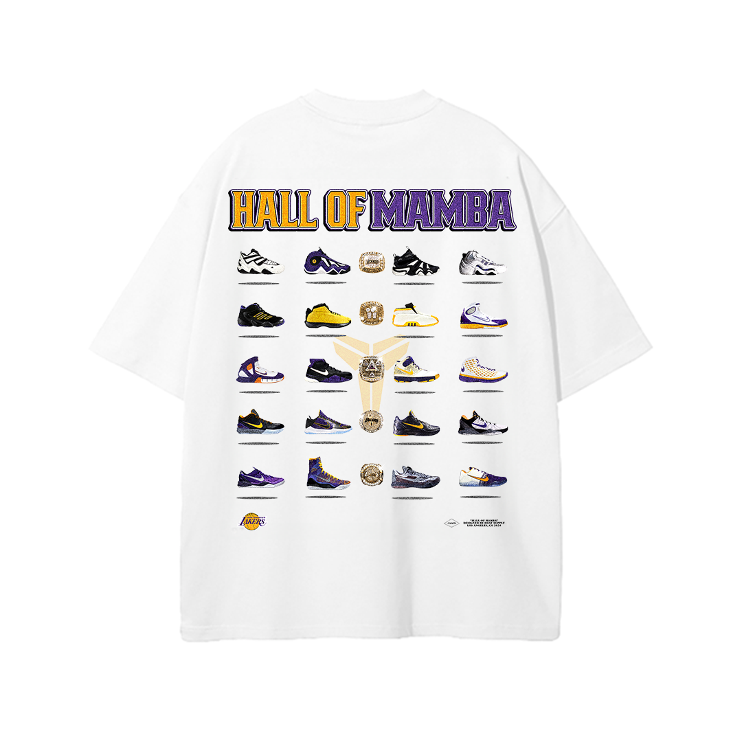 A white T-shirt with a design featuring various iconic Kobe Bryant sneakers arranged in a grid pattern along with his championship rings and a trophy. The text "Hall of Mamba" is displayed prominently at the top in purple and gold