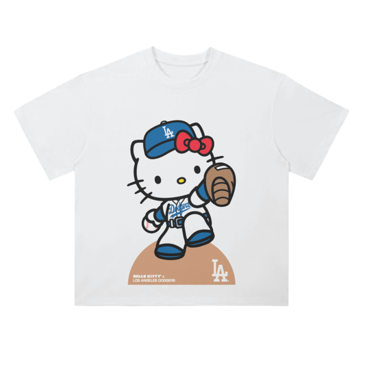 A white T-shirt with an image of Hello Kitty in a Los Angeles Dodgers uniform standing on a pitcher's mound, wearing a baseball glove, with the Dodgers logo on her chest and the LA Dodgers emblem on the mound