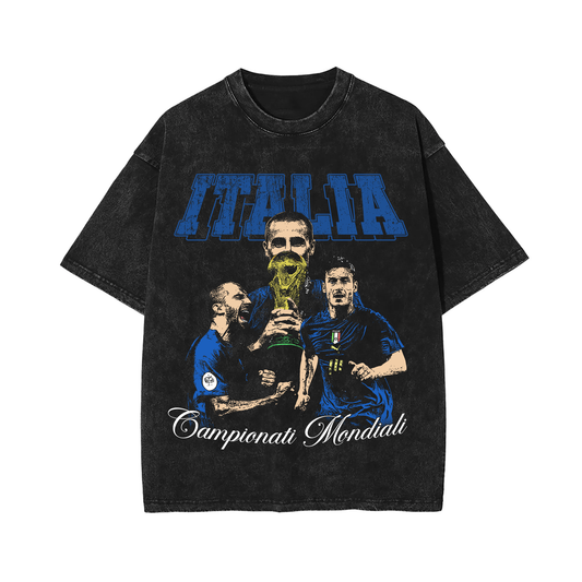 A vintage-style black acid wash T-shirt featuring the 2006 World Cup Champions of Italy. The design showcases three Italian players holding the World Cup trophy with "Italia" written in bold blue letters across the top. The distressed wash and oversized fit give the shirt a retro, streetwear vibe.