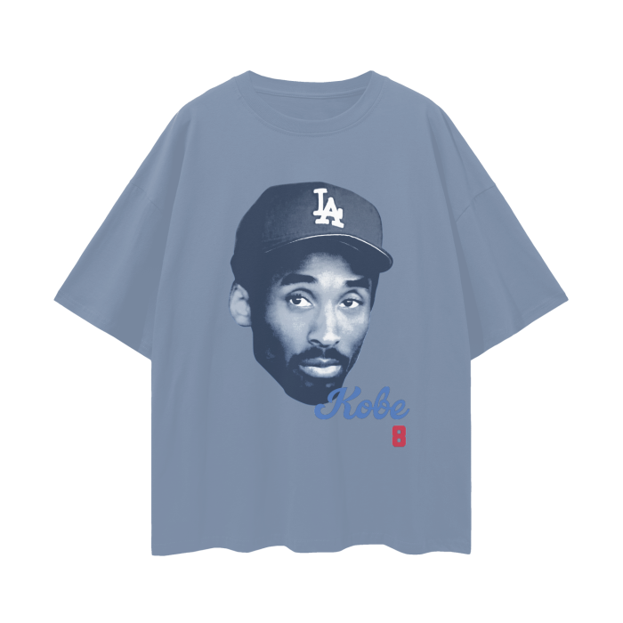 A blue oversized t-shirt featuring a large, monochromatic image of Kobe Bryant wearing an LA Dodgers baseball cap. The shirt has a minimalist design with the name "Kobe" in blue cursive and the number "8" in red beneath the image.