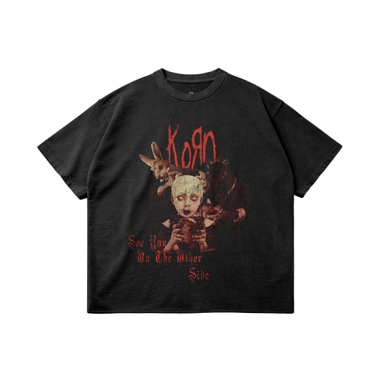 Black oversized T-shirt featuring a vintage-style graphic design of the band Korn. The front displays eerie, gothic illustrations with characters and the text 'Korn' in red, along with the words 'See You On The Other Side' at the bottom. The shirt has a worn, distressed look that complements its dark, alternative style