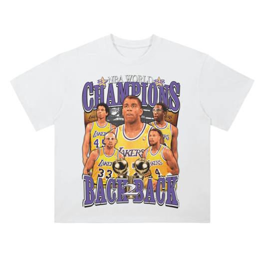 A white t-shirt featuring a retro design celebrating the Los Angeles Lakers' back-to-back NBA championships. The front of the t-shirt highlights the key players, including Magic Johnson and Kareem Abdul-Jabbar, with the phrase 'NBA World Champions' above and 'Back to Back' below. The design is done in purple and gold, with the players shown holding two championship trophies