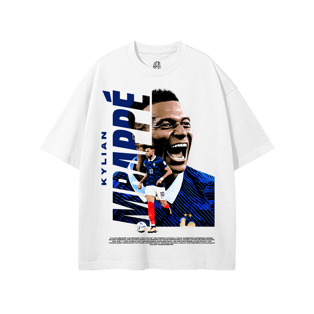 White heavyweight cotton standard fit T-shirt featuring an exclusive Kylian Mbappé graphic with bold vertical "MBAPPÉ" typography, a large portrait, action pose in the France national team kit, and blue Les Bleus-inspired graphics. Premium football streetwear design for France supporters.