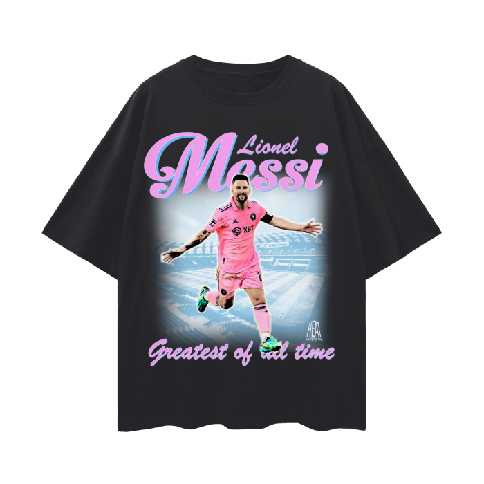A black oversized Lionel Messi soccer tee showing Messi in his pink Inter Miami jersey with the text "Lionel Messi - Greatest of All Time" written in pink and purple font.