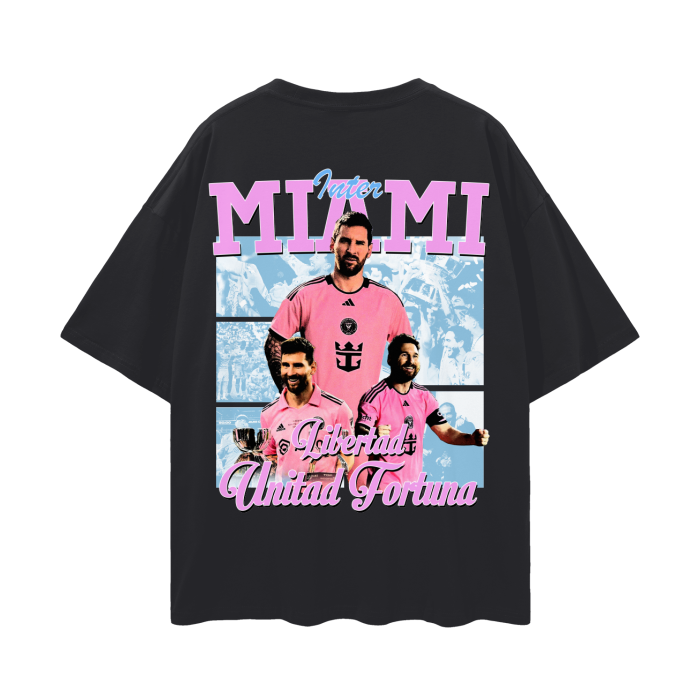 A black oversized Inter Miami soccer tee featuring Lionel Messi in a vibrant pink Inter Miami jersey with "Libertad Unidad Fortuna" written below the graphics, alongside images of Messi in different celebratory moments.