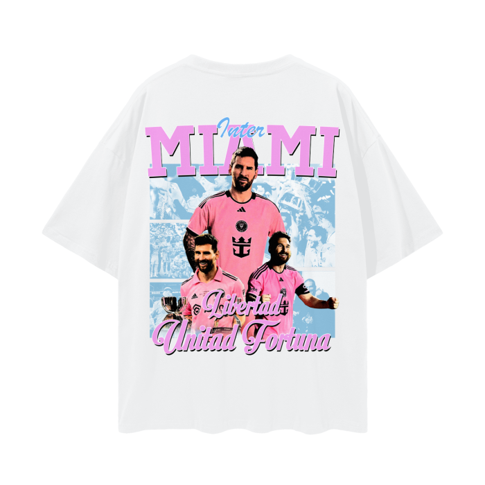 A white oversized Inter Miami soccer tee featuring Lionel Messi in a vibrant pink Inter Miami jersey with "Libertad Unidad Fortuna" written below the graphics, alongside images of Messi in different celebratory moments.