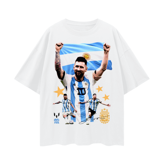 A white oversized t-shirt featuring multiple images of Lionel Messi, including him holding the Argentine flag, with gold stars and the FIFA and AFA logos.