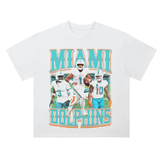 A white heavyweight drop shoulder t-shirt showcasing prominent Miami Dolphins players, including Tua Tagovailoa, in action poses on the front, with the text "MIAMI DOLPHINS" in large teal and orange letters at the top and bottom. Back