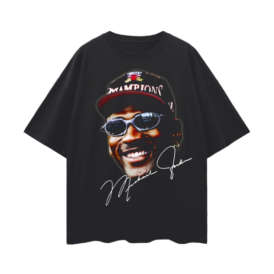  A black oversized T-shirt showcasing a close-up image of Michael Jordan smiling, wearing a championship hat and sunglasses. The design includes Jordan's signature in white at the bottom, emphasizing the celebratory and iconic moment.