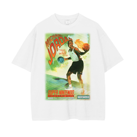A white oversized T-shirt featuring a vintage design inspired by Michael Jordan's "Chaos in the Windy City" Super Nintendo video game. The front showcases Michael Jordan in a dynamic pose holding two basketballs, one engulfed in flames, with vibrant retro colors and the Super Nintendo logo at the bottom.