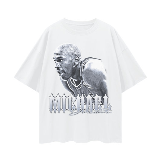 A white oversized tee featuring a grayscale image of Michael Jordan in action. The text "Michael Jordan" is displayed in bold, stylized lettering beneath the image. The tee has a loose fit with deep drop shoulders, giving it a casual, trendy vibe. Perfect for fans of the iconic basketball player and vintage-inspired fashion.