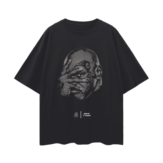 A black oversized t-shirt with a minimalist design showcasing a close-up of Mike Tyson's face, emphasizing his distinctive facial tattoo. The graphic portrays Tyson in a serious expression, with the branding of Alpha Industries and Mike Tyson displayed below.