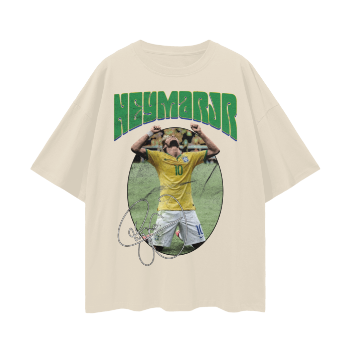 A cream colored oversized t-shirt featuring Neymar Jr. in a celebratory pose with his hands raised. The text "NEYMAR JR" is written in large green letters above the image, and his signature is displayed below the image.