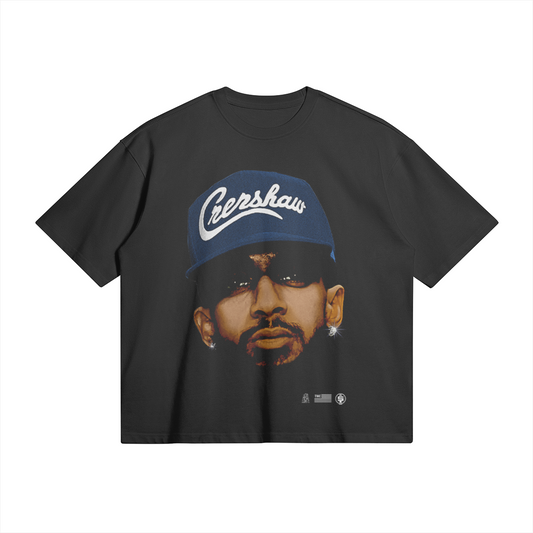 A black oversized heavyweight t-shirt featuring a large, detailed image of Nipsey Hussle's face. He is wearing a blue cap with the word "Crenshaw" written on it in white script. He is also wearing dark sunglasses and has diamond earrings.