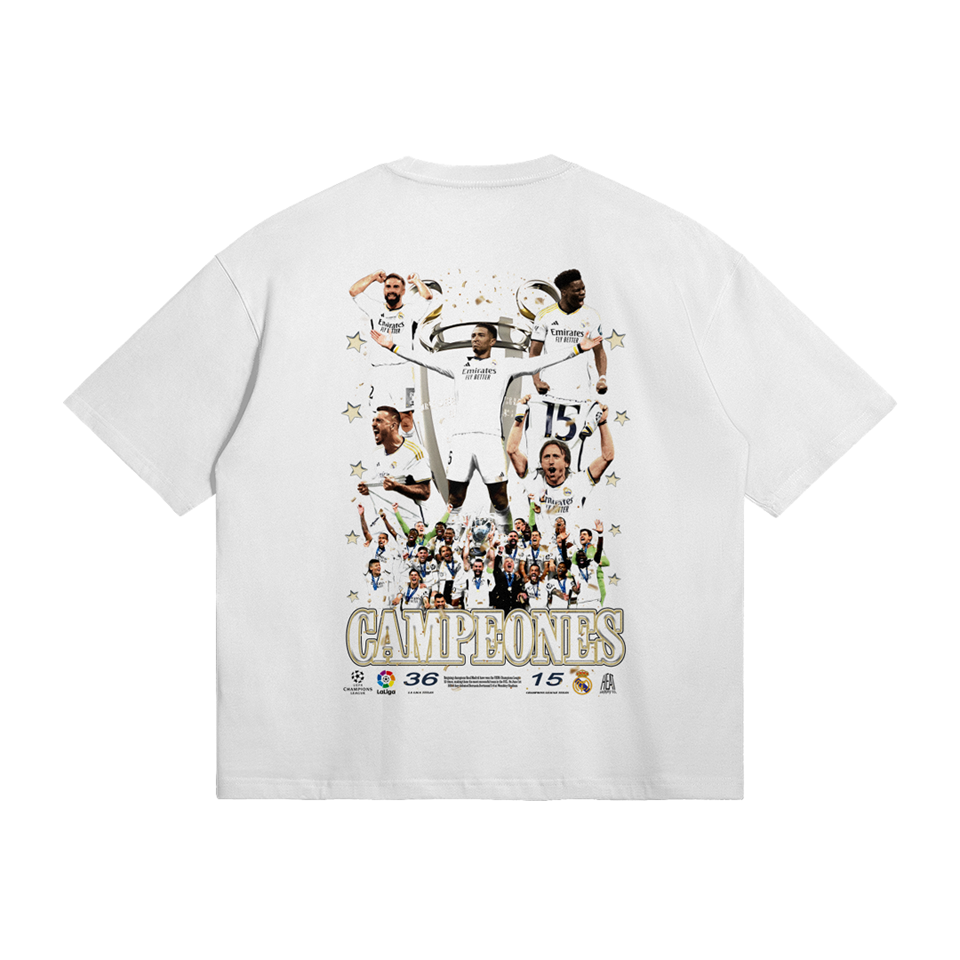 A white oversized t-shirt featuring a collage of Real Madrid players celebrating their Champions League victory. The word "CAMPEONES" is displayed prominently at the bottom in gold.