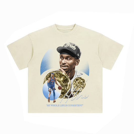 Cream-colored oversized unisex t-shirt with a large graphic of Shai Gilgeous-Alexander wearing a finals cap next to gold MVP trophies and action poses, with the phrase “MY WHOLE LIFE IS CONSISTENT” in light blue.