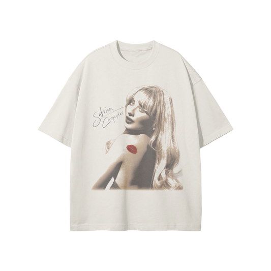 A cream-colored oversized t-shirt featuring a grayscale image of Sabrina Carpenter with a red lipstick kiss mark on her shoulder and her signature in black on the front