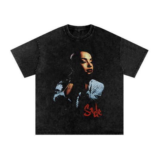Black acid-wash unisex t-shirt featuring a large graphic portrait of Sade with a polka-dot blouse, red lipstick, and the name “Sade” in bold red script near the hem.