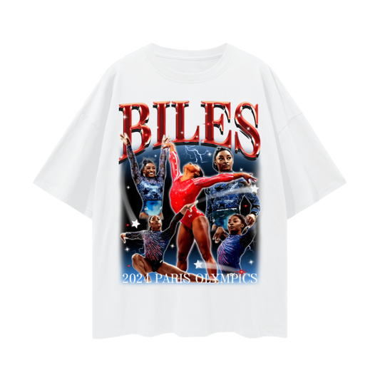 A white oversized t-shirt featuring a vibrant collage of Simone Biles in various gymnastic poses. The design prominently displays the name "BILES" in bold red letters at the top and includes the text "2024 Paris Olympics" at the bottom.