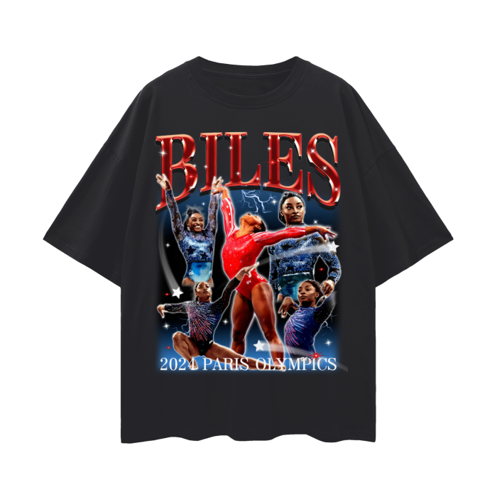 A black oversized t-shirt featuring a vibrant collage of Simone Biles in various gymnastic poses. The design prominently displays the name "BILES" in bold red letters at the top and includes the text "2024 Paris Olympics" at the bottom.